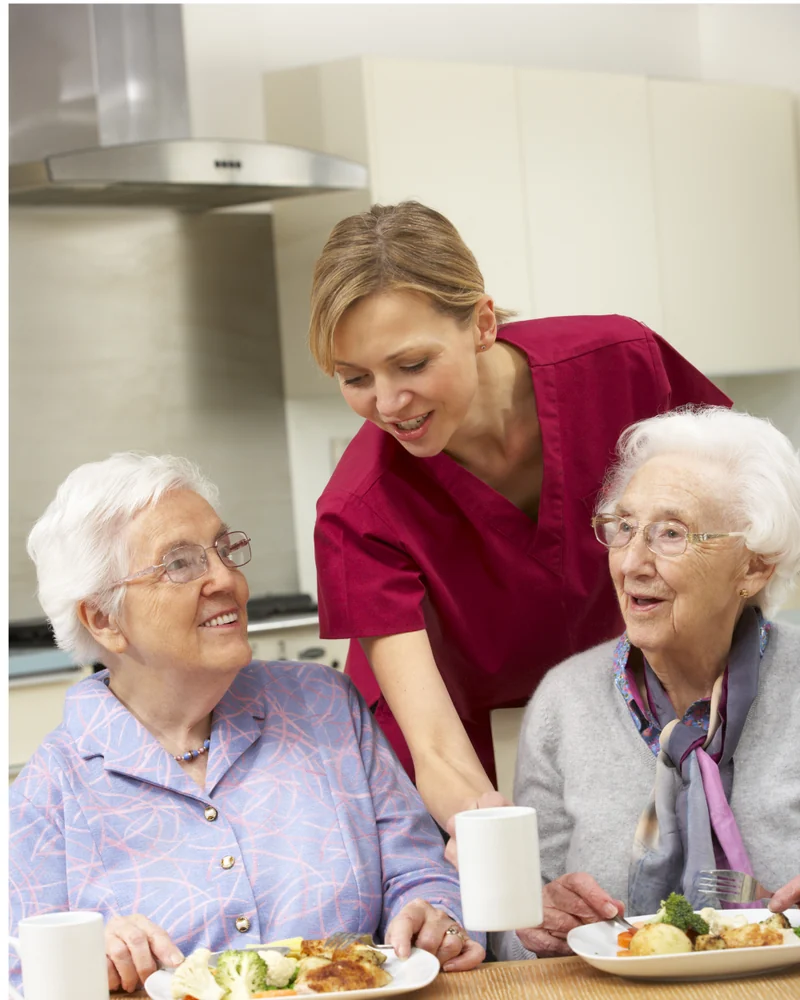 A carer sharing a warm meal and a chat with two older women